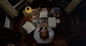 Movie still from “Throw Momma from the Train” (1987), directed by Danny DeVito – A man sitting at a table with a typewriter; Medium shot, Overhead angle