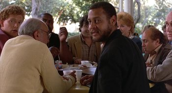 Movie still from “Throw Momma from the Train” (1987), directed by Danny DeVito – A group of people sitting at a table with food; Medium shot, Over the shoulder angle