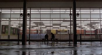 Movie still from “Throw Momma from the Train” (1987), directed by Danny DeVito – Two people are sitting on a bench in the rain; Extreme Wide shot, Low angle
