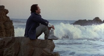 Movie still from “Throw Momma from the Train” (1987), directed by Danny DeVito – A man sitting on top of a rock near the ocean; Wide shot, Low angle