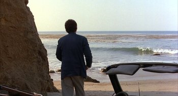 Movie still from “Throw Momma from the Train” (1987), directed by Danny DeVito – A man standing on the beach looking out at the ocean; Extreme Wide shot, High angle