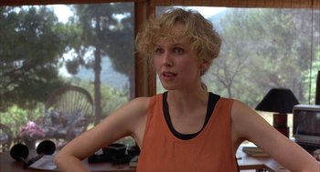 Movie still from “Throw Momma from the Train” (1987), directed by Danny DeVito – A woman with blonde curly hair wearing an orange tank top; Close Up shot, Over the shoulder angle