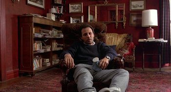 Movie still from “Throw Momma from the Train” (1987), directed by Danny DeVito – A man sitting in a chair in a living room; Medium shot, High angle