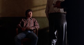 Movie still from “Throw Momma from the Train” (1987), directed by Danny DeVito – A man sitting on a chair in a room; Medium shot, Low angle