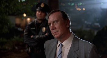 Movie still from “Throw Momma from the Train” (1987), directed by Danny DeVito – A man in a suit and tie next to a police officer; Close Up shot, Over the shoulder angle