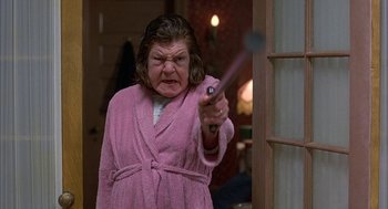 Movie still from “Throw Momma from the Train” (1987), directed by Danny DeVito – A woman in a pink bathrobe holding a gun; Close Up shot, High angle