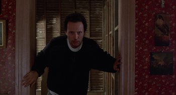 Movie still from “Throw Momma from the Train” (1987), directed by Danny DeVito – A man leaning against a wall in a dark room; Medium shot, Low angle