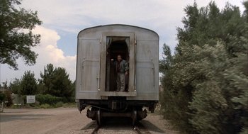 Movie still from “Throw Momma from the Train” (1987), directed by Danny DeVito – A man standing on the side of an old train car; Wide shot, Low angle