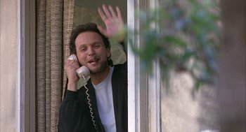 Movie still from “Throw Momma from the Train” (1987), directed by Danny DeVito – A man holding a phone to his ear while standing in front of a window; Medium shot, Low angle