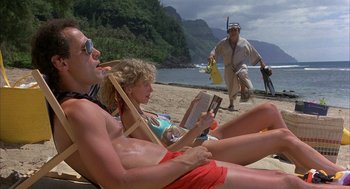 Movie still from “Throw Momma from the Train” (1987), directed by Danny DeVito – Two people sitting on the beach reading a book; Wide shot, Over the shoulder angle