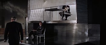 Movie still from “Thunderball” (1965), directed by Terence Young – A man sitting in a chair in front of a desk; Wide shot, Low angle