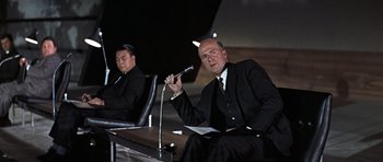 Movie still from “Thunderball” (1965), directed by Terence Young – A man in a suit and tie holding a microphone; Medium shot, Low angle