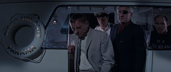 Movie still from “Thunderball” (1965), directed by Terence Young – A man wearing a suit and tie standing next to two other men; Medium shot, Low angle