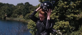 Movie still from “Thunderball” (1965), directed by Terence Young – A woman in a leather jacket holding a helmet on top of her head; Medium shot, Low angle