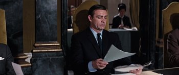 Movie still from “Thunderball” (1965), directed by Terence Young – A man sitting at a table with papers in front of him; Medium shot, Low angle