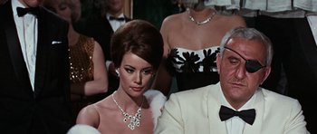 Movie still from “Thunderball” (1965), directed by Terence Young – A woman in a white dress sitting next to a man in a suit; Medium shot, Over the shoulder angle