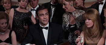 Movie still from “Thunderball” (1965), directed by Terence Young – A man in a suit and tie next to a woman in a black dress; Medium shot, High angle