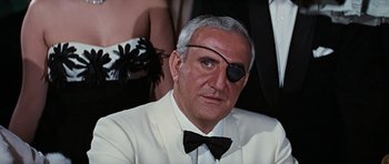Movie still from “Thunderball” (1965), directed by Terence Young – An older man wearing a white suit and a black bow tie; Close Up shot, Over the shoulder angle