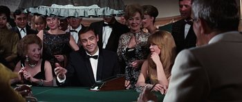 Movie still from “Thunderball” (1965), directed by Terence Young – A group of men and women sitting around a table; Medium shot, Over the shoulder angle