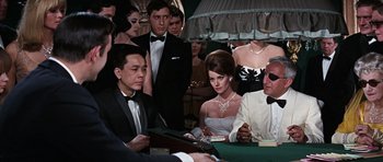 Movie still from “Thunderball” (1965), directed by Terence Young – A group of people sitting at a table in a room; Medium shot, Over the shoulder angle