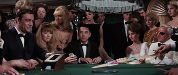 Movie still from “Thunderball” (1965), directed by Terence Young – A man sitting at a poker table with people standing around him; Medium shot, High angle