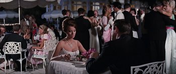 Movie still from “Thunderball” (1965), directed by Terence Young – A woman sitting at a dinner table with a man; Medium shot, High angle