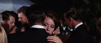 Movie still from “Thunderball” (1965), directed by Terence Young – A man and a woman hugging each other in front of a group of people; Close Up shot, Over the shoulder angle
