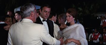 Movie still from “Thunderball” (1965), directed by Terence Young – A group of people standing next to each other in formal wear; Medium shot, Over the shoulder angle