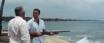 Movie still from “Thunderball” (1965), directed by Terence Young – A man holding a rifle near the water; Medium shot, Low angle