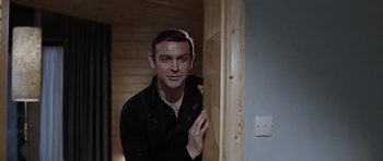 Movie still from “Thunderball” (1965), directed by Terence Young – A man in black shirt leaning against a wooden wall; Medium shot, Low angle