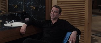 Movie still from “Thunderball” (1965), directed by Terence Young – A man in a black shirt sitting in a chair; Medium shot, High angle