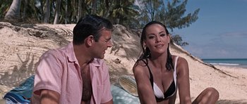 Movie still from “Thunderball” (1965), directed by Terence Young – A man and a woman sitting next to each other on the beach; Medium shot, Over the shoulder angle
