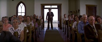 Movie still from “Thunderbolt and Lightfoot” (1974), directed by Michael Cimino – A group of people sitting in a room with a man in a suit and hat; Wide shot, Low angle