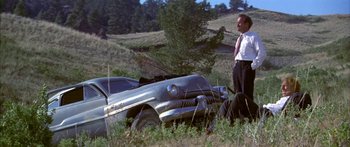 Movie still from “Thunderbolt and Lightfoot” (1974), directed by Michael Cimino – A man standing next to an old car in a field; Wide shot, Low angle