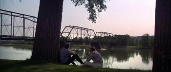 Movie still from “Thunderbolt and Lightfoot” (1974), directed by Michael Cimino – Two people sitting next to each other near a river; Wide shot, Over the shoulder angle
