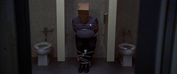 Movie still from “Thunderbolt and Lightfoot” (1974), directed by Michael Cimino – A police officer tied to a wall in a bathroom; Wide shot, Overhead angle