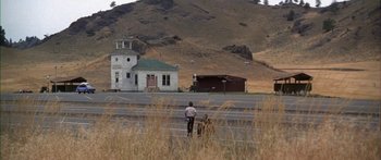 Movie still from “Thunderbolt and Lightfoot” (1974), directed by Michael Cimino – A man standing on a road in front of a building; Extreme Wide shot, High angle