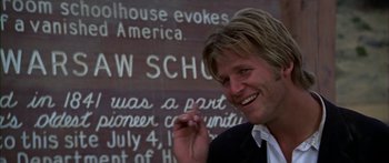 Movie still from “Thunderbolt and Lightfoot” (1974), directed by Michael Cimino – A person smiling near a sign; Close Up shot, Low angle