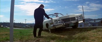 Movie still from “Thunderbolt and Lightfoot” (1974), directed by Michael Cimino – A man standing next to a white car in a field; Wide shot, Low angle