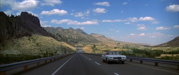 Movie still from “Thunderbolt and Lightfoot” (1974), directed by Michael Cimino – A car driving down a road with mountains in the background; Extreme Wide shot, High angle