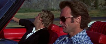 Movie still from “Thunderbolt and Lightfoot” (1974), directed by Michael Cimino – Two men sitting in a red car , one of them wearing sunglasses; Close Up shot, Over the shoulder angle
