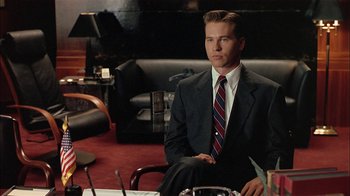 Movie still from “Thunderheart” (1992), directed by Michael Apted – A man in a suit sitting in front of papers; Medium shot, Over the shoulder angle