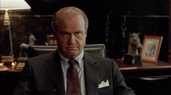 Movie still from “Thunderheart” (1992), directed by Michael Apted – An older man wearing a suit and tie sitting in a chair; Close Up shot, Low angle