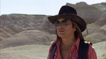 Movie still from “Thunderheart” (1992), directed by Michael Apted – A man with long hair wearing sunglasses and a cowboy hat; Close Up shot, Over the shoulder angle