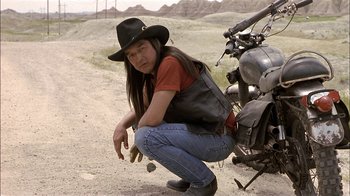 Movie still from “Thunderheart” (1992), directed by Michael Apted – A man kneeling down next to a parked motorcycle; Medium shot, Low angle