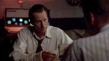 Movie still from “Thunderheart” (1992), directed by Michael Apted – A man sitting at a table in a room; Close Up shot, Over the shoulder angle