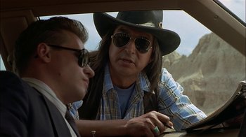 Movie still from “Thunderheart” (1992), directed by Michael Apted – A man in a cowboy hat sitting next to another man; Close Up shot, Over the shoulder angle