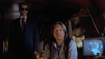 Movie still from “Thunderheart” (1992), directed by Michael Apted – A man with long black hair sitting next to another man in a suit; Medium shot, Over the shoulder angle