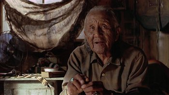 Movie still from “Thunderheart” (1992), directed by Michael Apted – An older man sitting in a room with a book; Close Up shot, Low angle