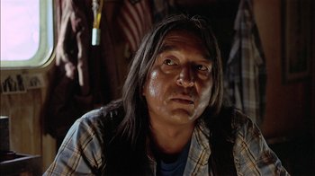 Movie still from “Thunderheart” (1992), directed by Michael Apted – A man with long black hair wearing a plaid shirt; Close Up shot, Low angle